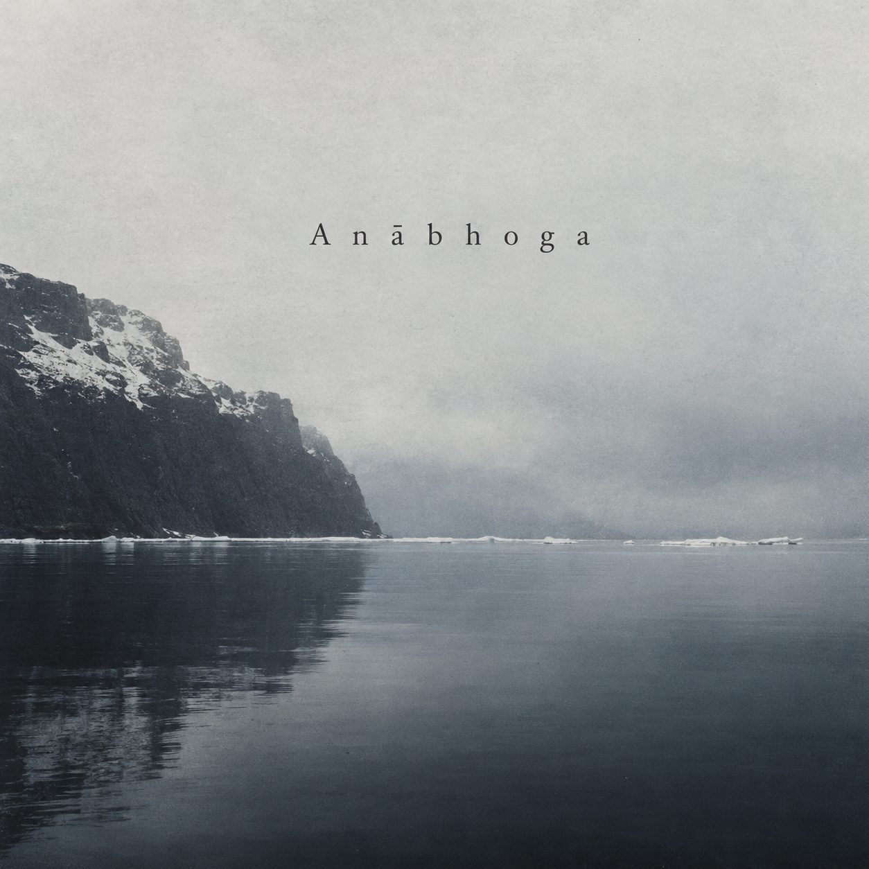 Black-and-white photograph of a dark, snow-streaked cliff dropping into still, mist-covered arctic water, ice floes on the far shore, and an enormous pale sky above.